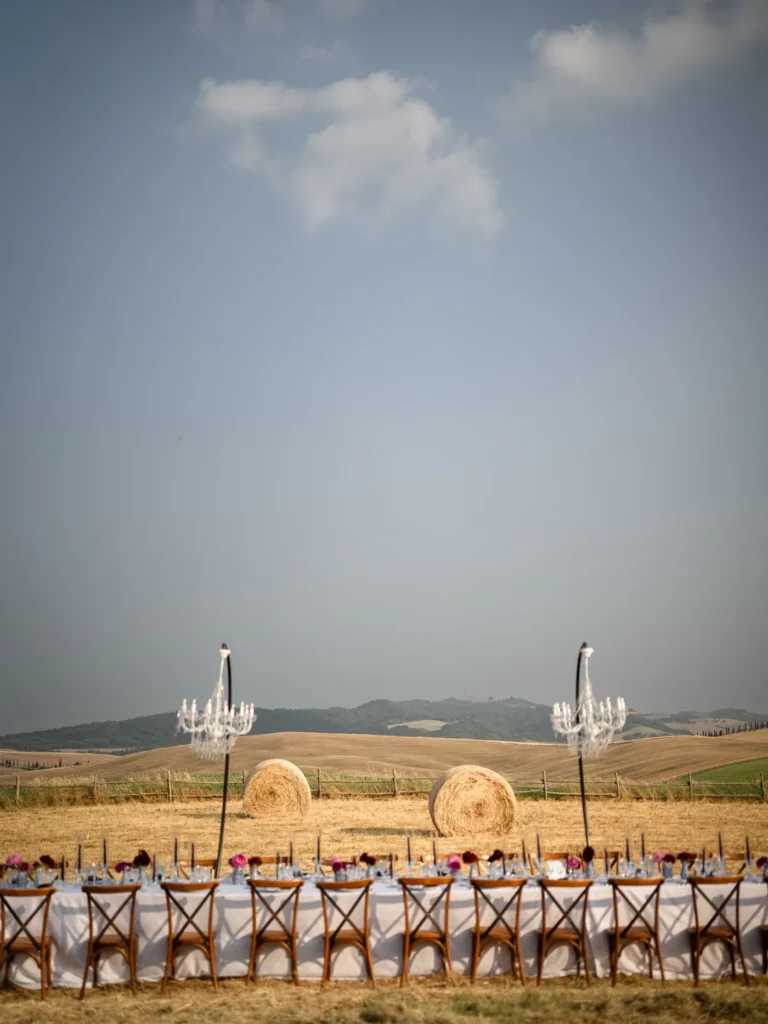 A long table with chandeliers and hay bales in the open field