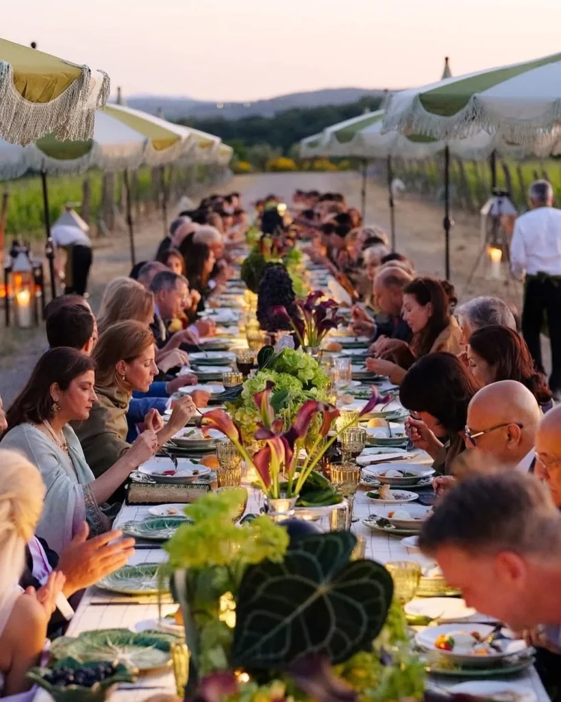 Guests at a long dinner table among the vines at sunset